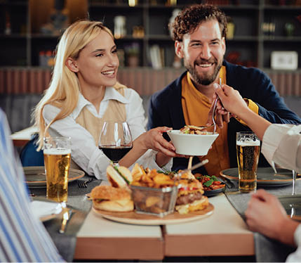 Multiethnic friends sitting at restaurant, drinking alcohol, chatting and having burgers for dinner.