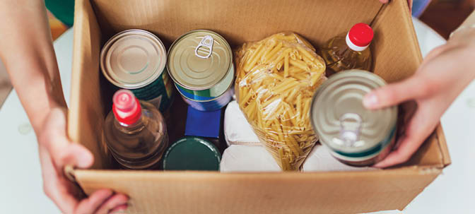 A person is holding a box filled with food items, including canned goods and pasta. AI generated content