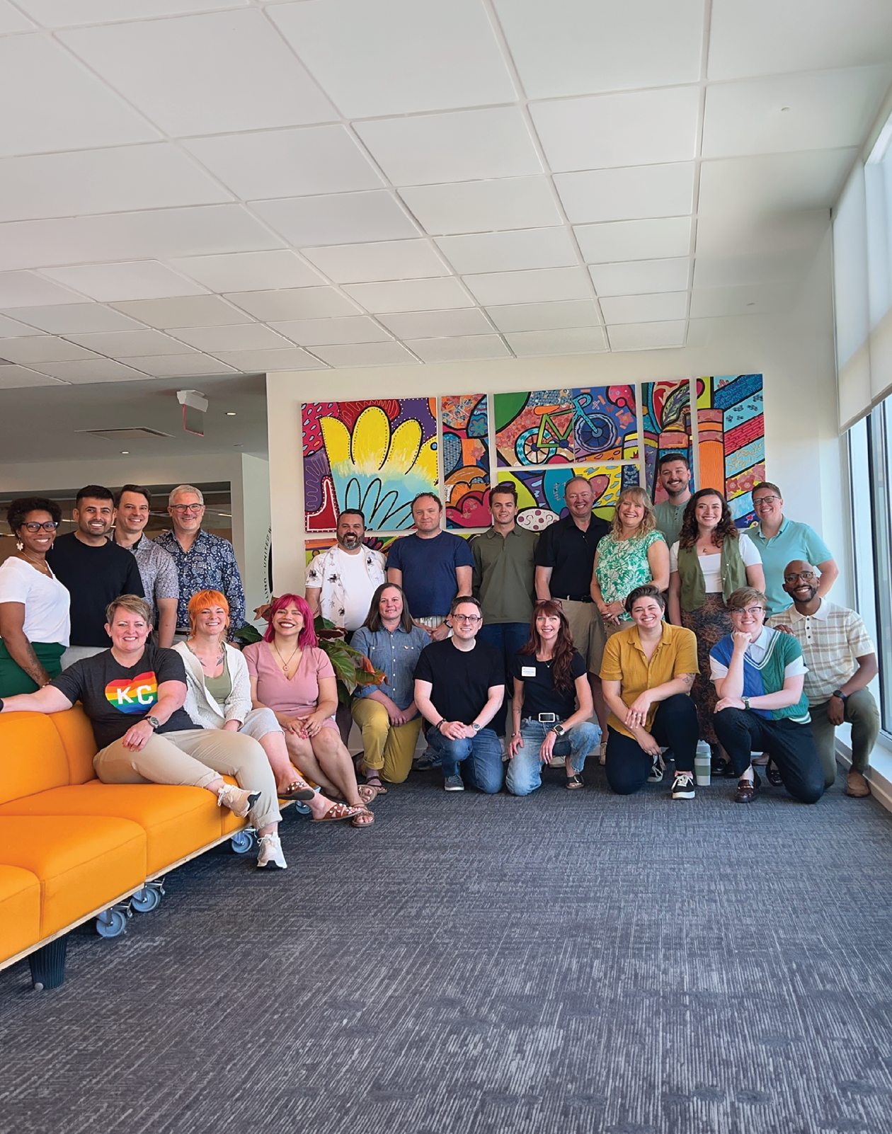 A group of people sitting on a couch in front of a colorful painting. Description generated by AI