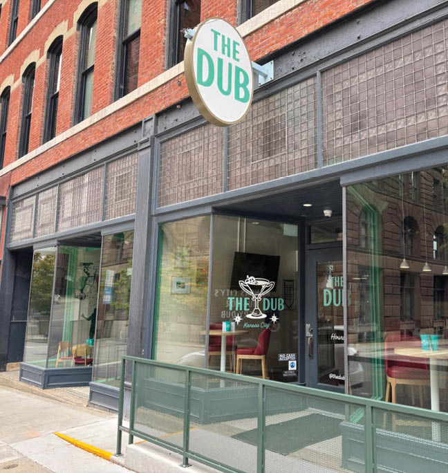 A restaurant with a green awning and a window with a sign that says “The Dub". Description generated by AI