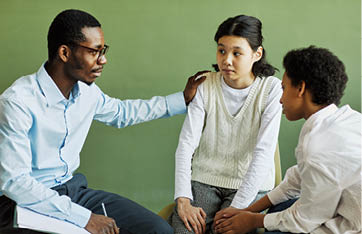 Young African American male psychologist supporting Asian schoolgirl and giving her advice at session while keeping hand on her shoulder