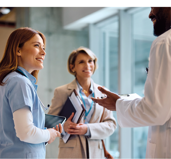 Happy nurse and African American doctor talking to a businesswoman in hallway of a medical clinic.