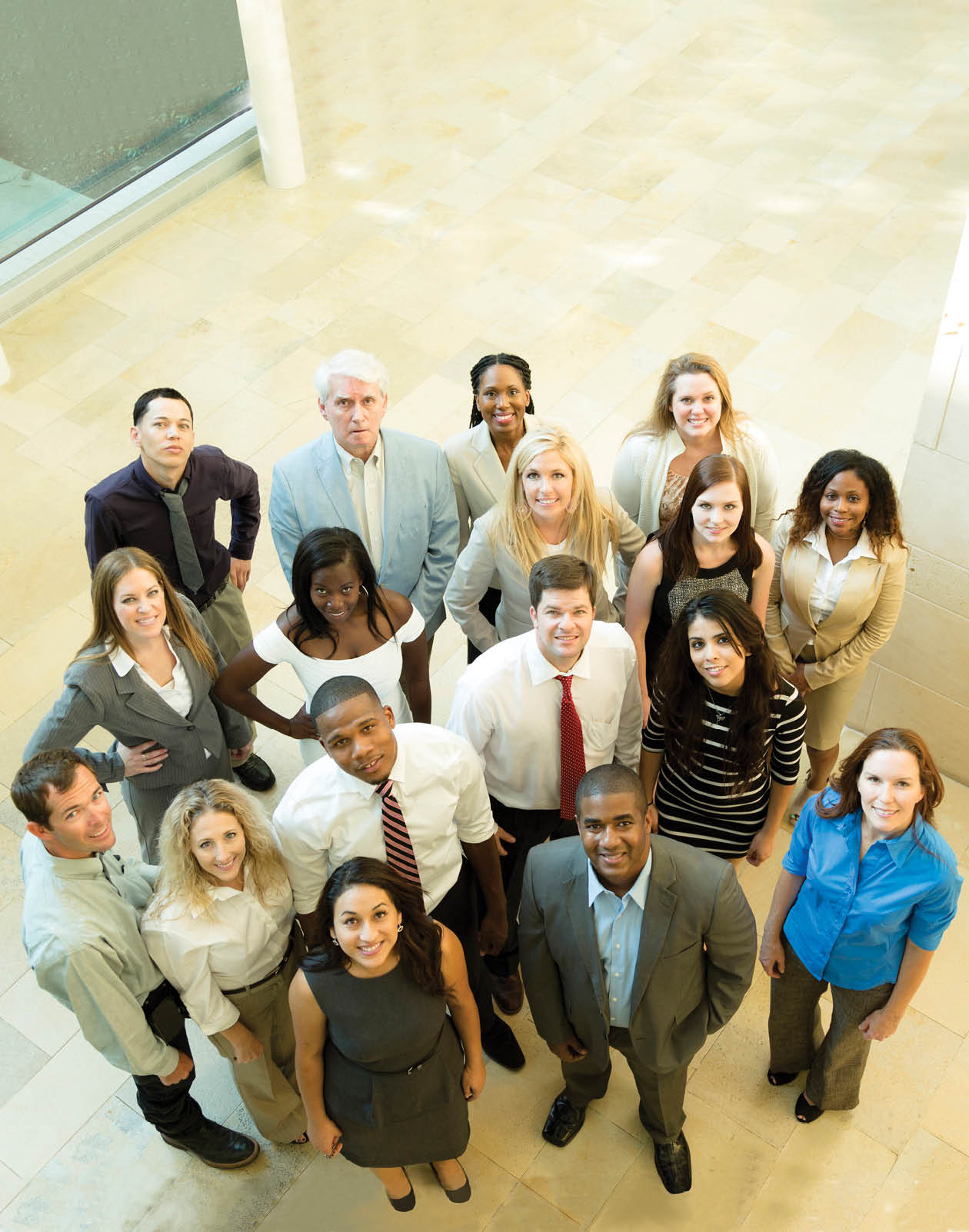 Multi-ethnic and mixed ages group of business people standing in office lobby area of building. They are looking up at camera. High-angle view.