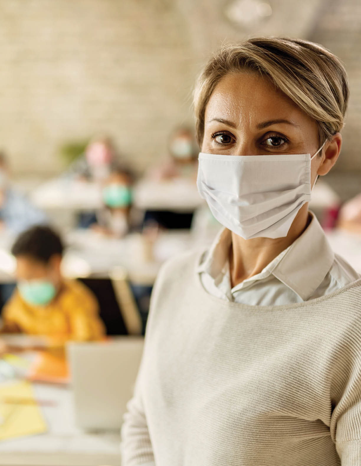Female teacher wearing a face mask while teaching children at elementary school and looking at camera 