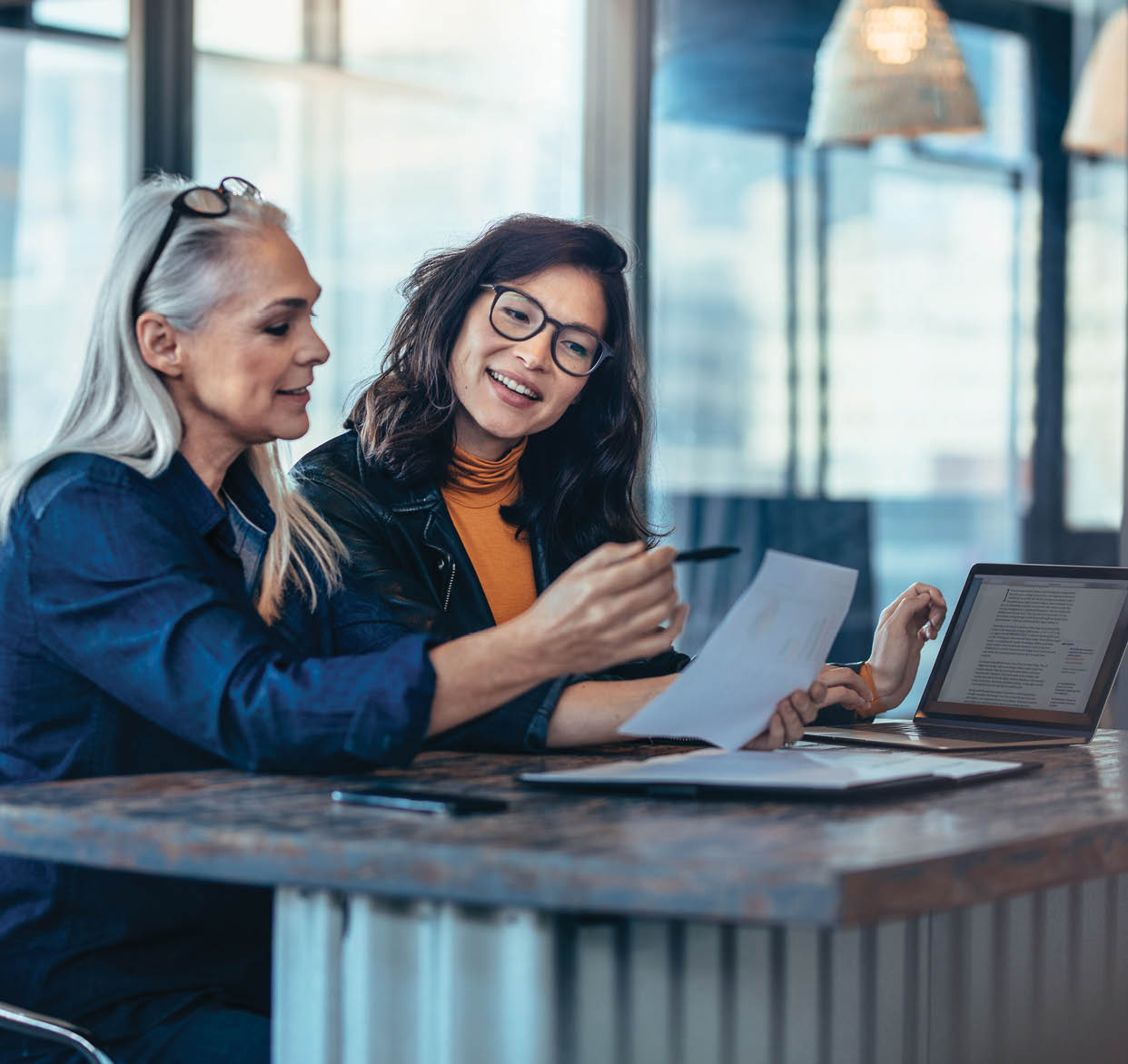 Two women analyzing documents while sitting on a table in office. Woman executives at work in office discussing some paperwork.