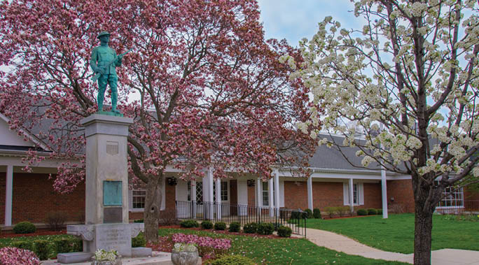 A statue of a man is in front of a building with a tree in the background. Description generated by AI