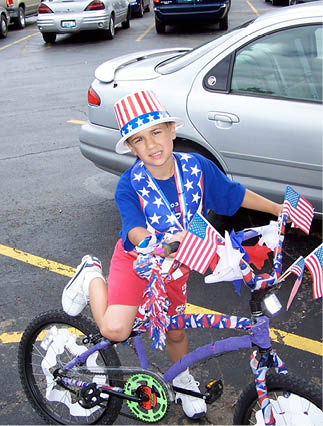 A boy wearing a red, white, and blue hat and shirt is sitting on a bicycle. Description generated by AI