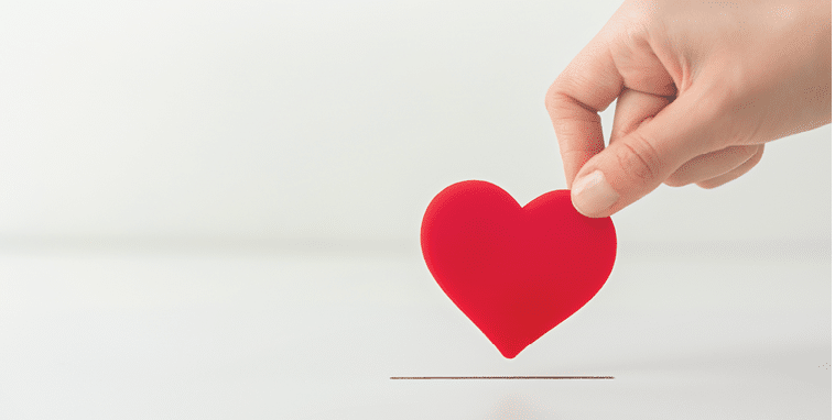 The concept of charity, love, donate and helping hand. Woman’s hand places heart in the donation slot. Donor of blood or human organs, saving lives.