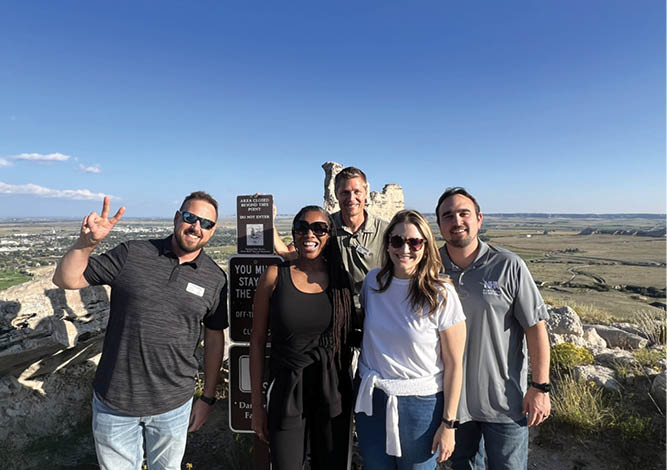 Four people are standing on a hill, posing for a picture. They are wearing sunglasses and smiling. AI generated content