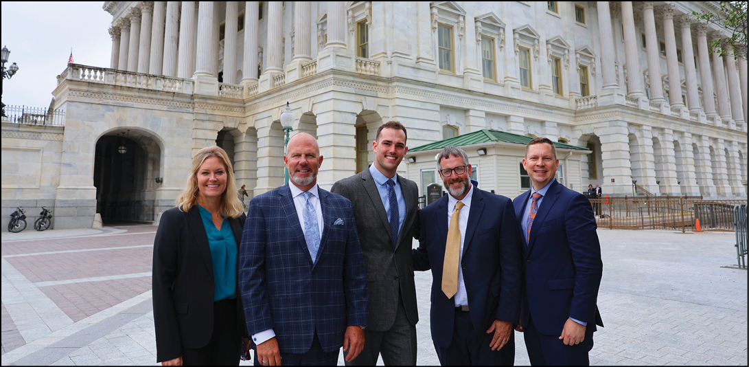Five people in suits pose in front of a large building. AI generated content