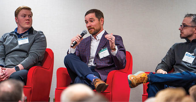 Three men are sitting on red chairs, with one of them speaking into a microphone. They are wearing suits and ties, and the man speaking appears to be gesturing with his hands. The other two men are listening attentively. AI generated content