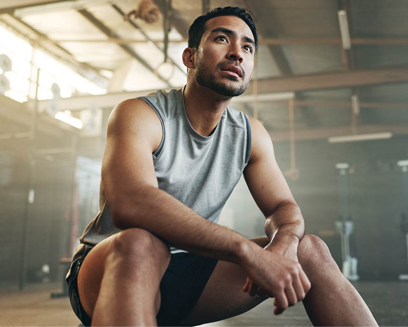 Fitness, breathing and sweating with a tired man in the gym, resting after an intense workout. Exercise, health and fatigue with a young athlete in recovery from training for sports or wellness