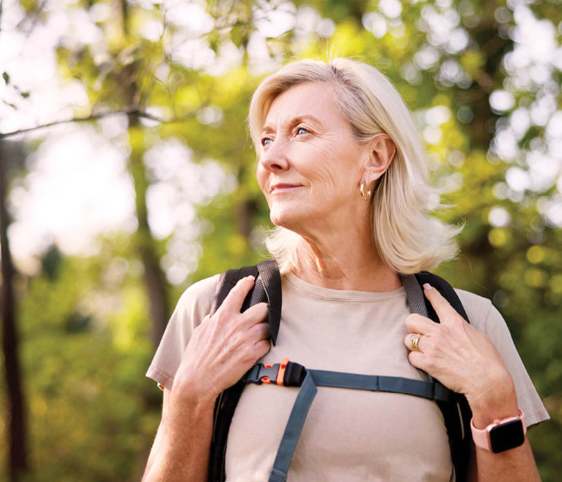 Mature, woman and hiking in forest with backpack for fitness adventure, sightseeing and explore nature. Trekking, person and thinking of scenery in woods with walking, holiday travel and cardio hobby
