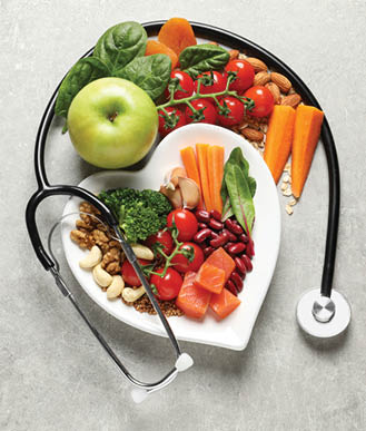 Overhead view of a heart-shaped plate containing a balanced diet rich in protein, fiber, and vitamins, including carrots, broccoli, tomatoes, apple, walnuts, and fish. A doctor's stethoscope is draped around the plate on a textured gray background, symbolizing cardiovascular wellness and dietary health. Perfect for articles on nutrition, cardiology, preventative medicine, and healthy lifestyle promotions.