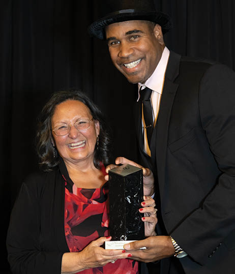 A man and woman are standing next to each other, both holding an award. The woman is wearing a red dress and the man is wearing a suit. AI generated content