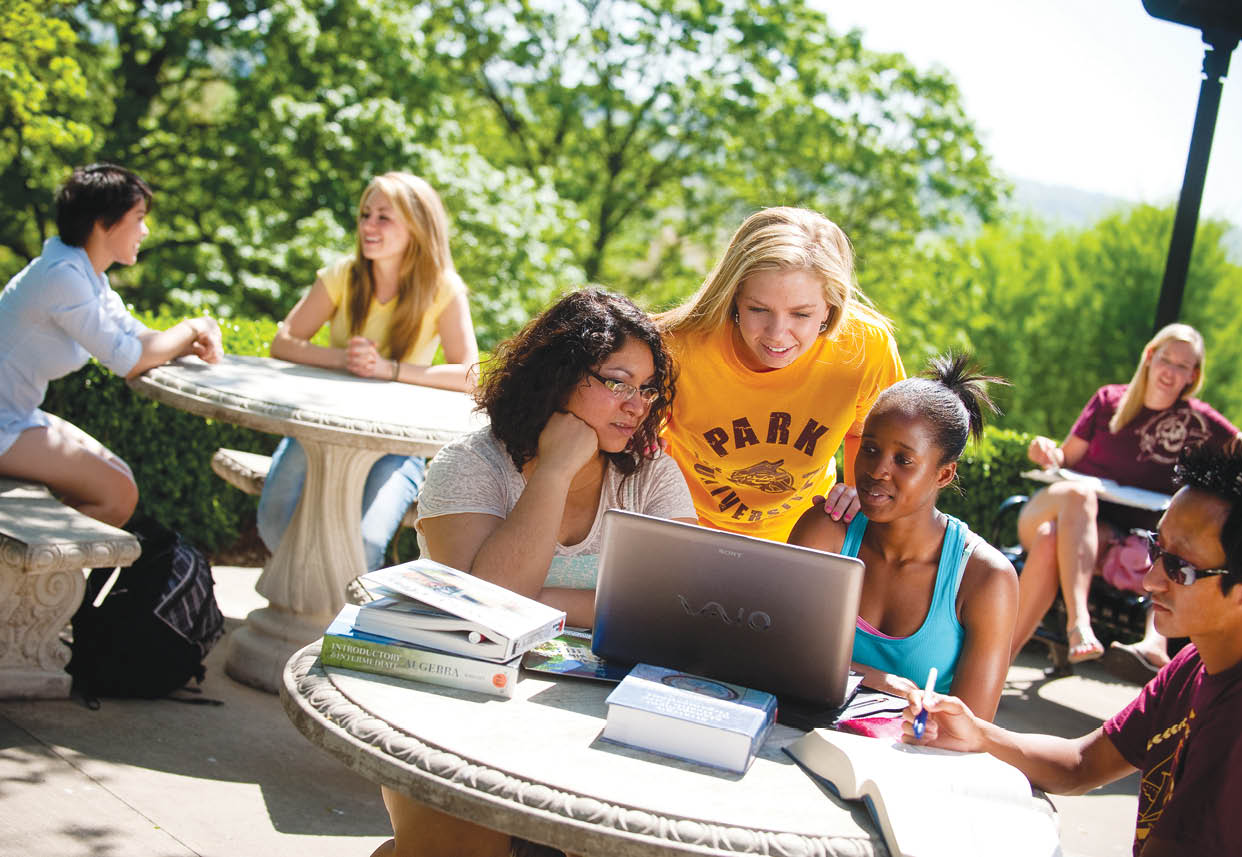 A group of people are sitting around a table with books and laptops. A woman is showing a laptop to a group of girls. AI generated content