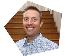 A man is smiling at the camera, wearing a blue shirt with white buttons. AI generated content
