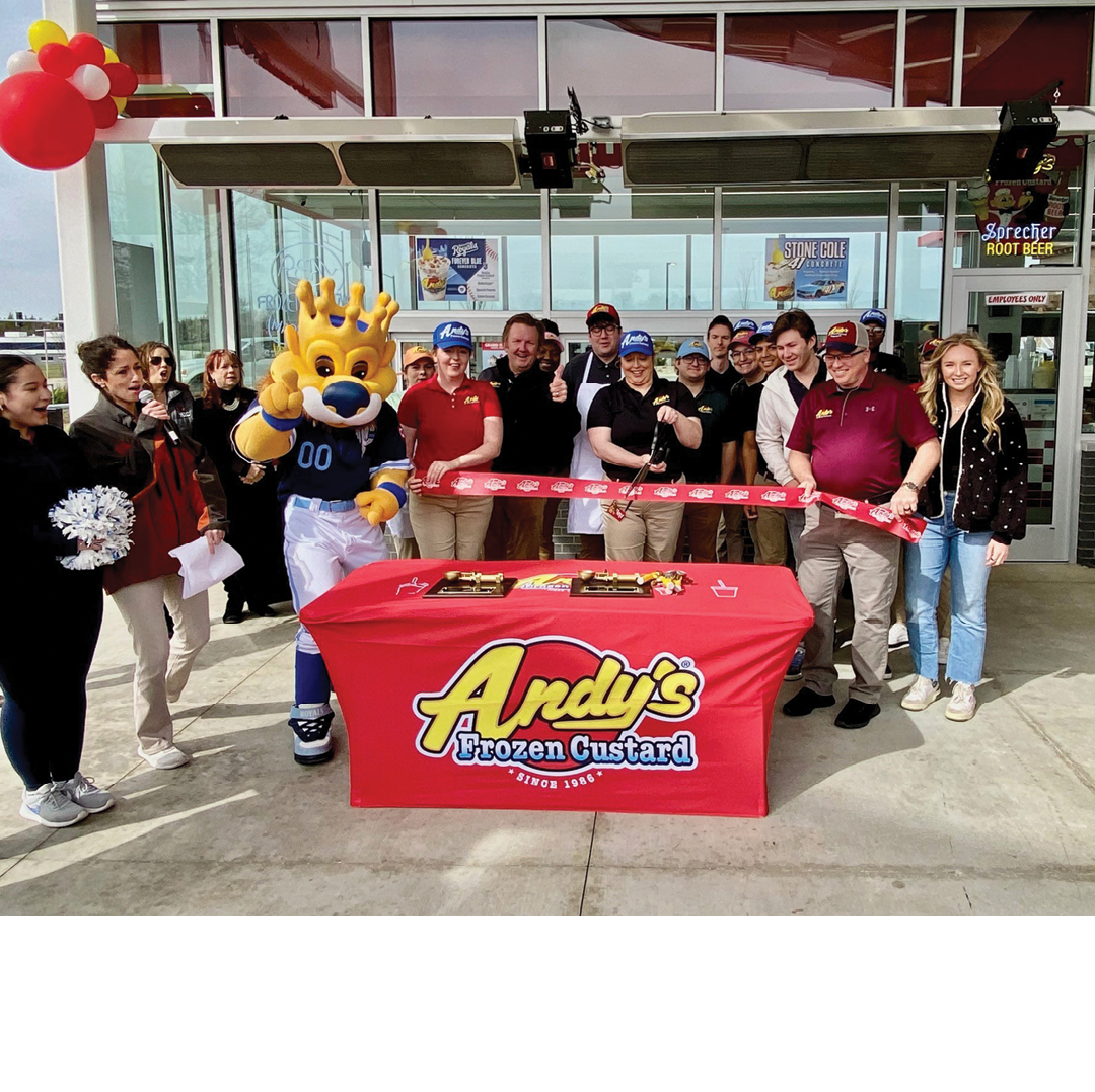 A group of people are standing in front of a red table with a sign that says “Andy's Frozen Custard." A mascot is present, holding a red ribbon. AI generated content