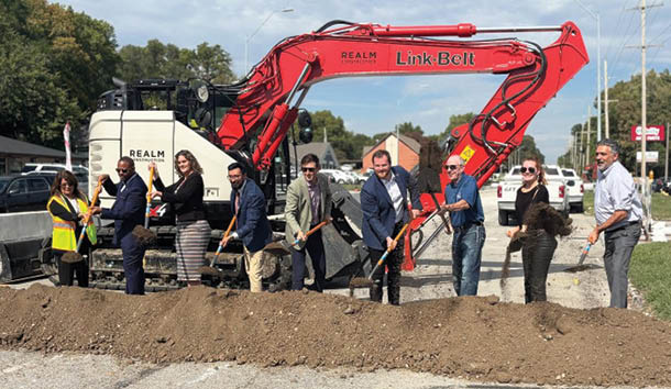 A group of people are standing around a pile of dirt, posing for a picture. They are wearing hard hats, indicating that they are construction workers. The scene is set on a street, with several cars parked nearby. AI generated content