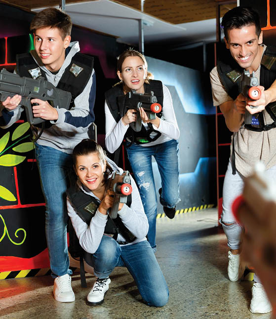 Modern positive smiling young people with laser pistols playing laser tag on dark labyrinth