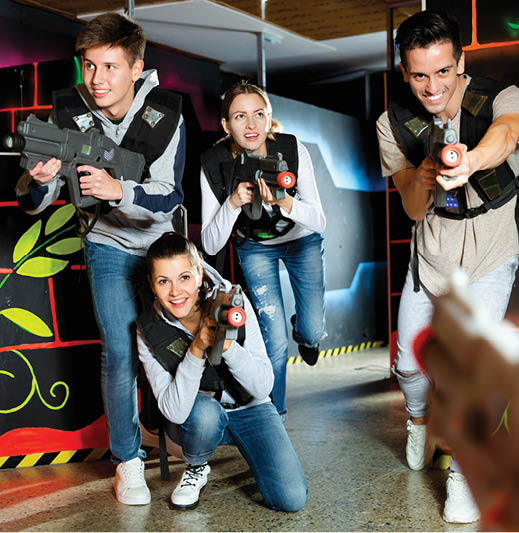 Modern positive smiling young people with laser pistols playing laser tag on dark labyrinth