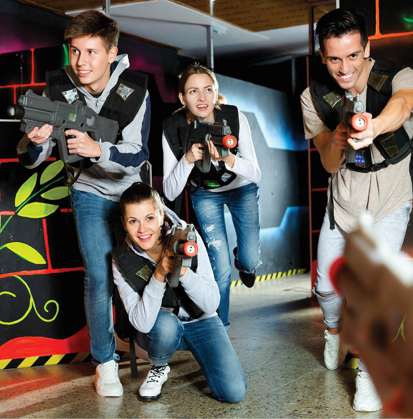 Modern positive smiling young people with laser pistols playing laser tag on dark labyrinth