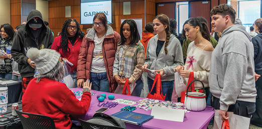 A group of people are gathered around a table with a woman sitting at it. The woman is handing out items to the people in the crowd. AI generated content