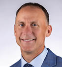 A man wearing a blue suit and tie smiles for the camera. AI generated content