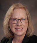 A woman wearing glasses and a black jacket smiles for the camera. AI generated content