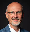 A man wearing a blue jacket and tie is smiling for the camera. AI generated content