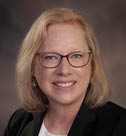A woman wearing glasses and a black jacket smiles for the camera. AI generated content