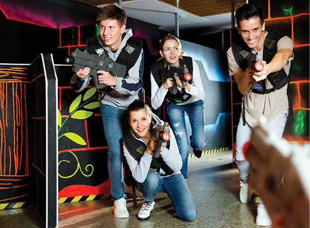 Modern positive smiling young people with laser pistols playing laser tag on dark labyrinth