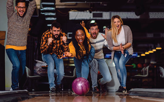 Group of friends enjoying time together laughing and cheering while bowling at club.