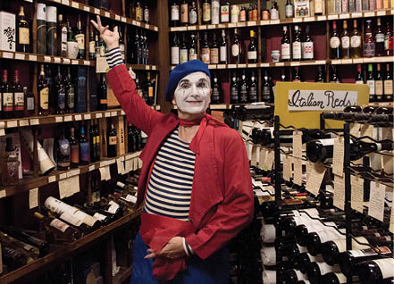 A person in a red jacket and a white and black face mask standing in a store with a lot of bottles. Description generated by AI