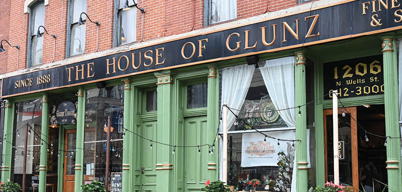 A green building with a sign that says “The House of Glunz & Co.". Description generated by AI