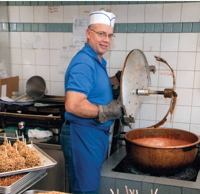 A man wearing a blue shirt and a white hat is standing in a kitchen. Description generated by AI