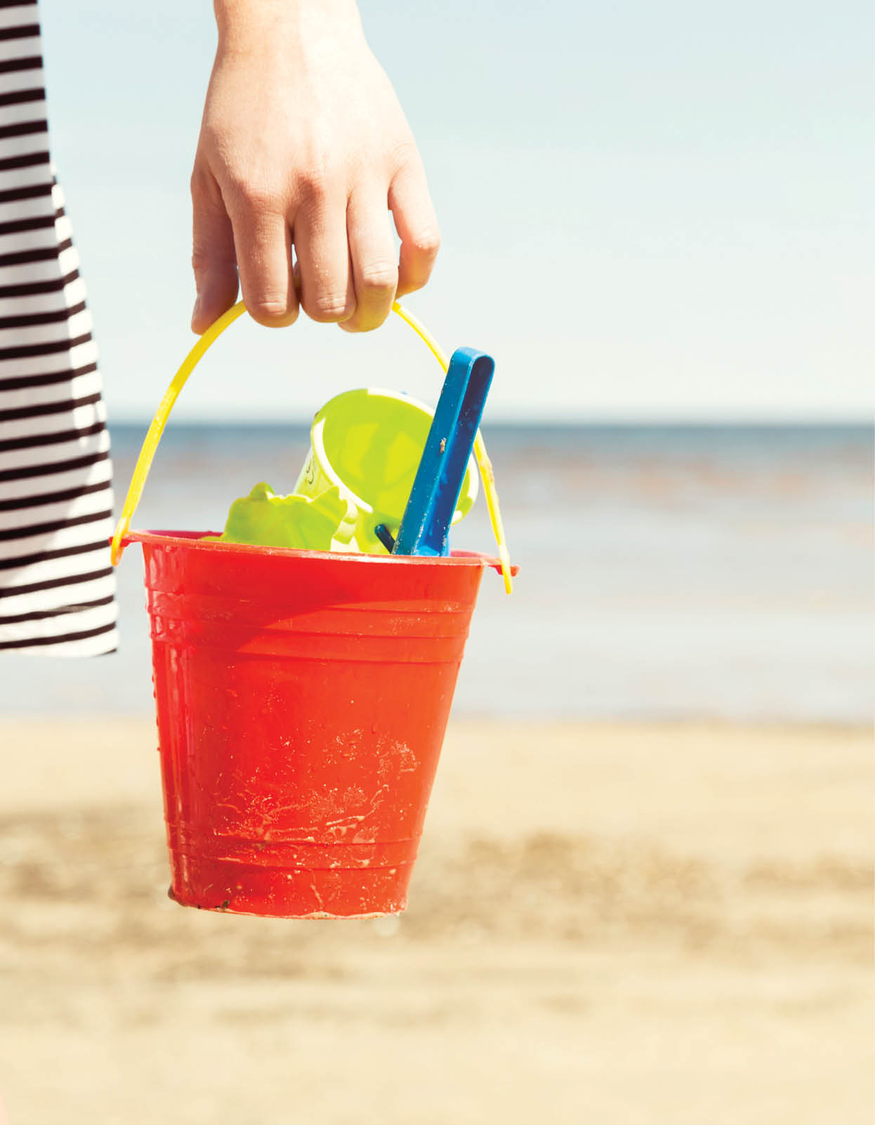 Woman holding bucket with children's beach toys - spade and shovel on a sunny day