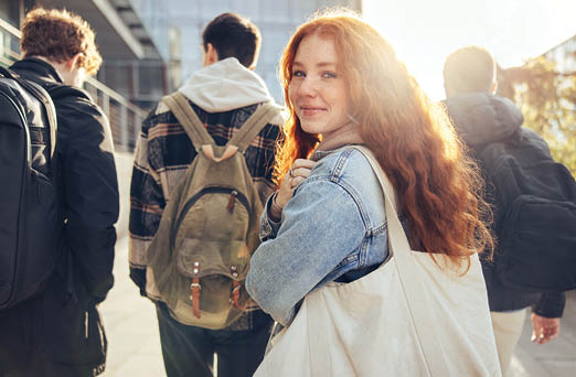 Female student glancing back while going for a class in college. Girl walking with friends going for class in high school.