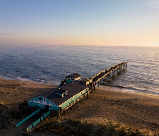 An aerial look at the Avalon Fishing Pier in Kill Devil Hills, North Carolina as the sun rises over the Atlantic Ocean