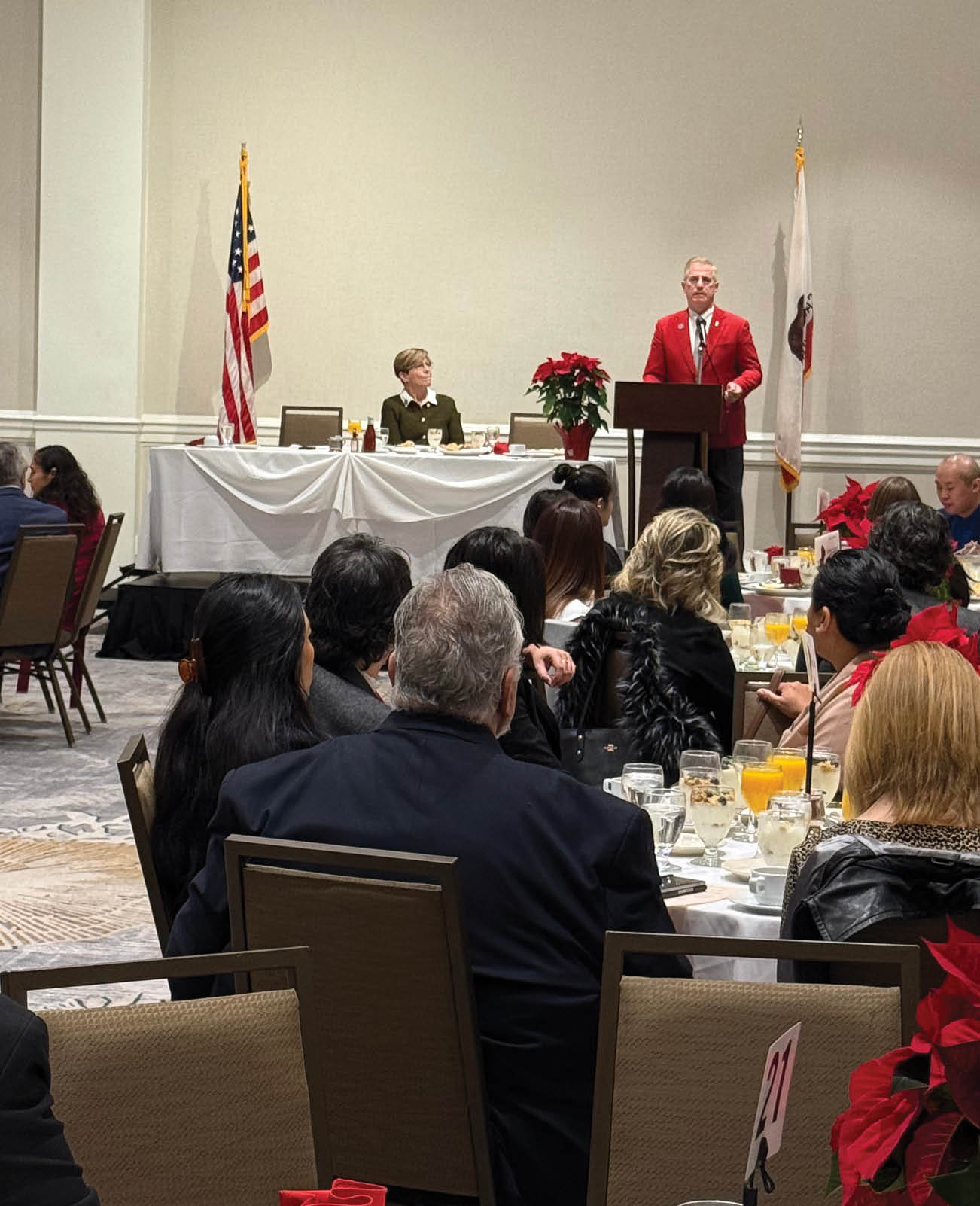 A man in a red shirt is speaking at a podium. Description generated by AI