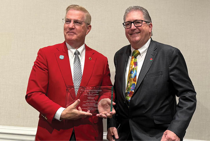 A man in a red jacket holds a plaque. Description generated by AI