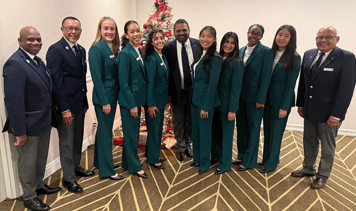 A group of people wearing green jackets and black pants. Description generated by AI