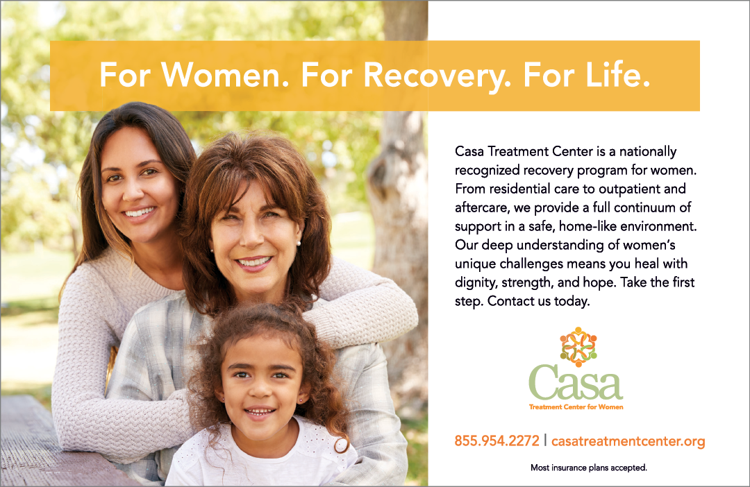 A woman holding a child in front of a sign that says “For Women, For Recovery, For Life." Description generated by AI