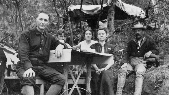 A group of people sitting around a table in a wooded area. Description generated by AI