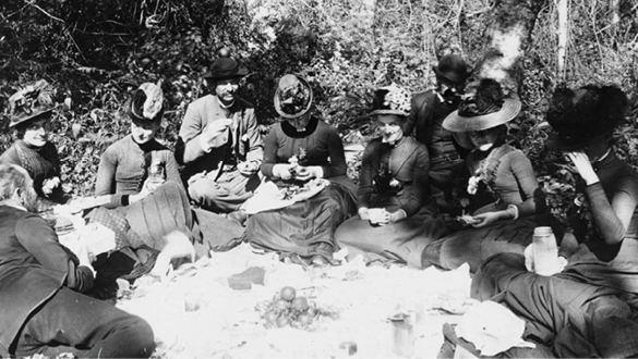 A group of people sitting around a table in a forest. Description generated by AI