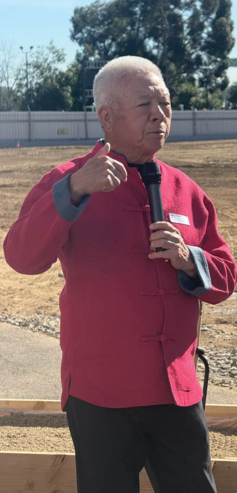 A man in a red shirt and black pants is holding a microphone. Description generated by AI
