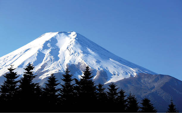 A snow covered mountain with trees in the foreground. Description generated by AI