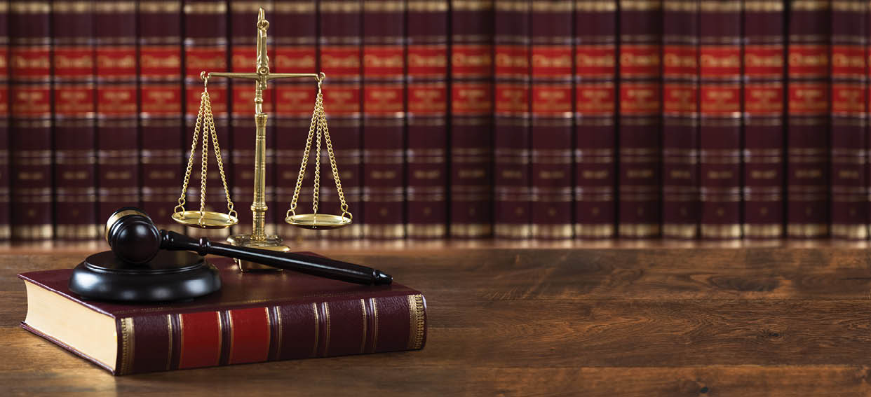 Closeup of mallet and legal book with justice scale on table in courtroom