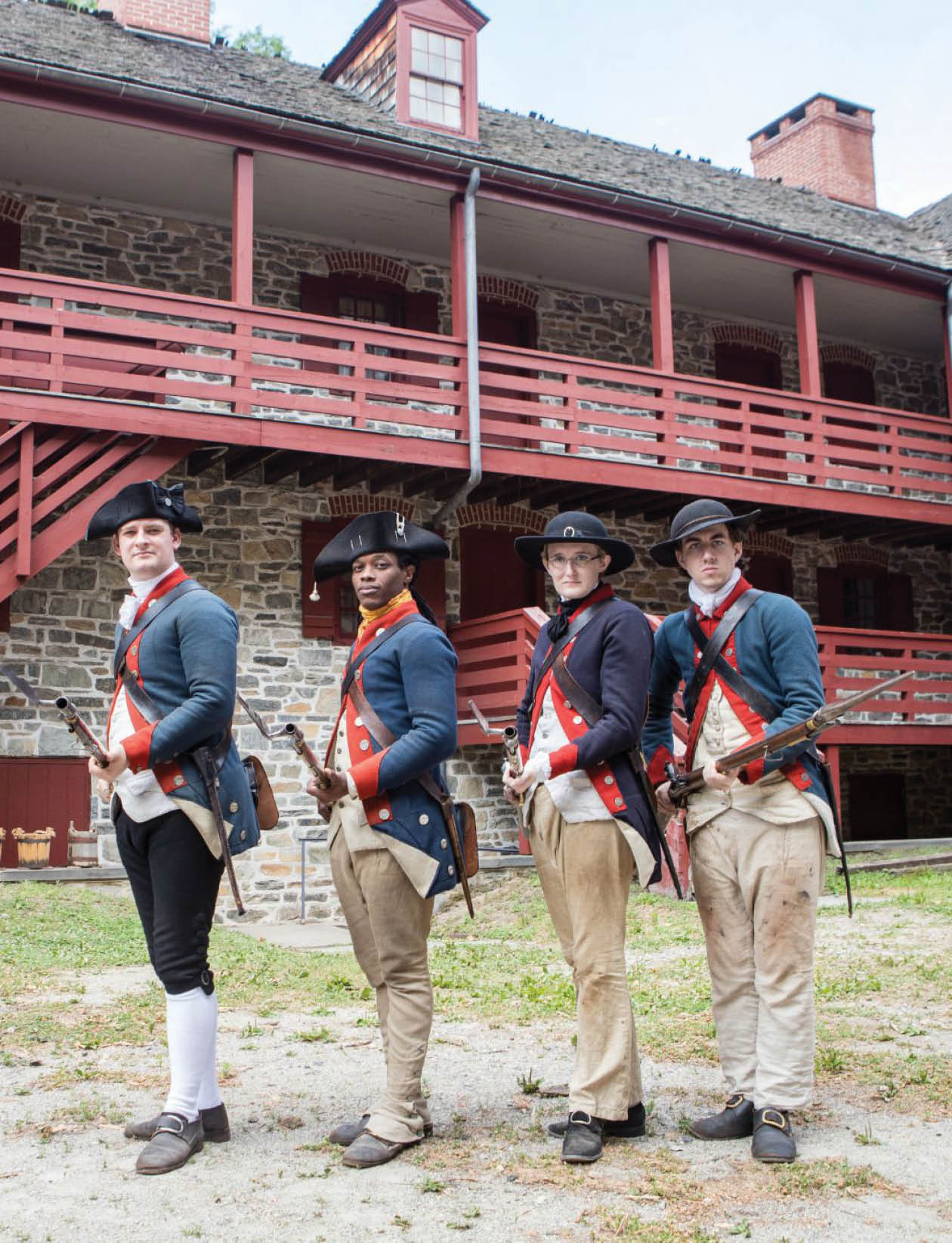 Four men in colonial attire are standing in front of a building. Description generated by AI
