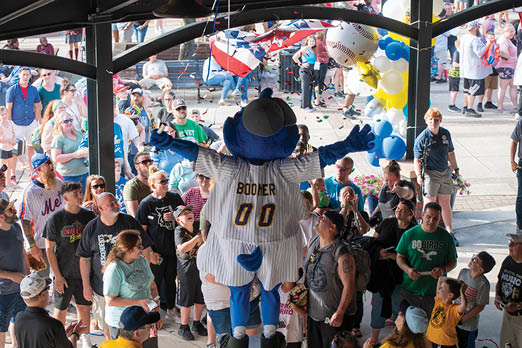 A crowd of people are gathered around a mascot dressed as a baseball player. Description generated by AI
